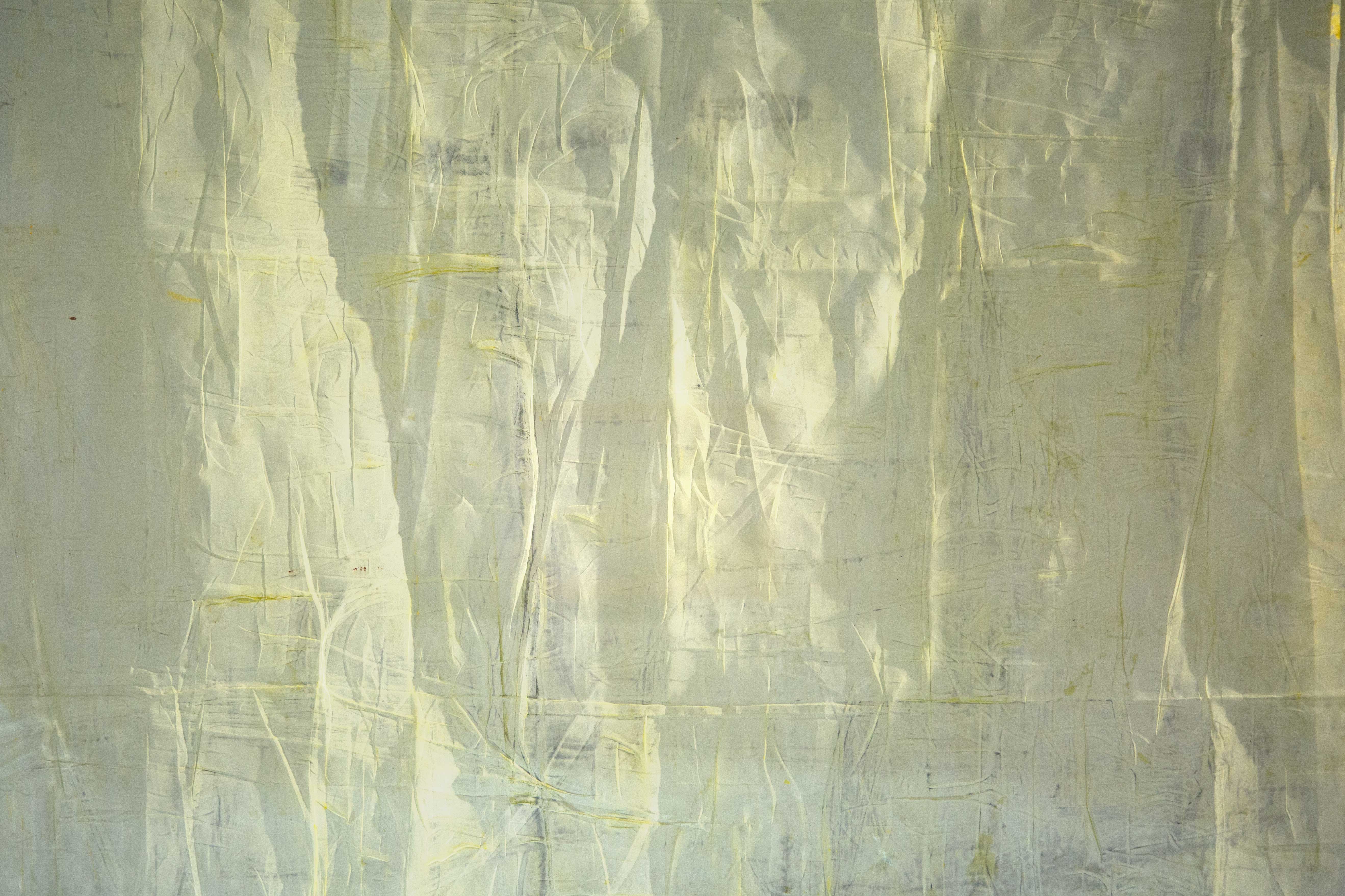 A close up detail photograph of a lightly yellow painted translucent cloth with light hitting its folds and creating dynamic shadows.