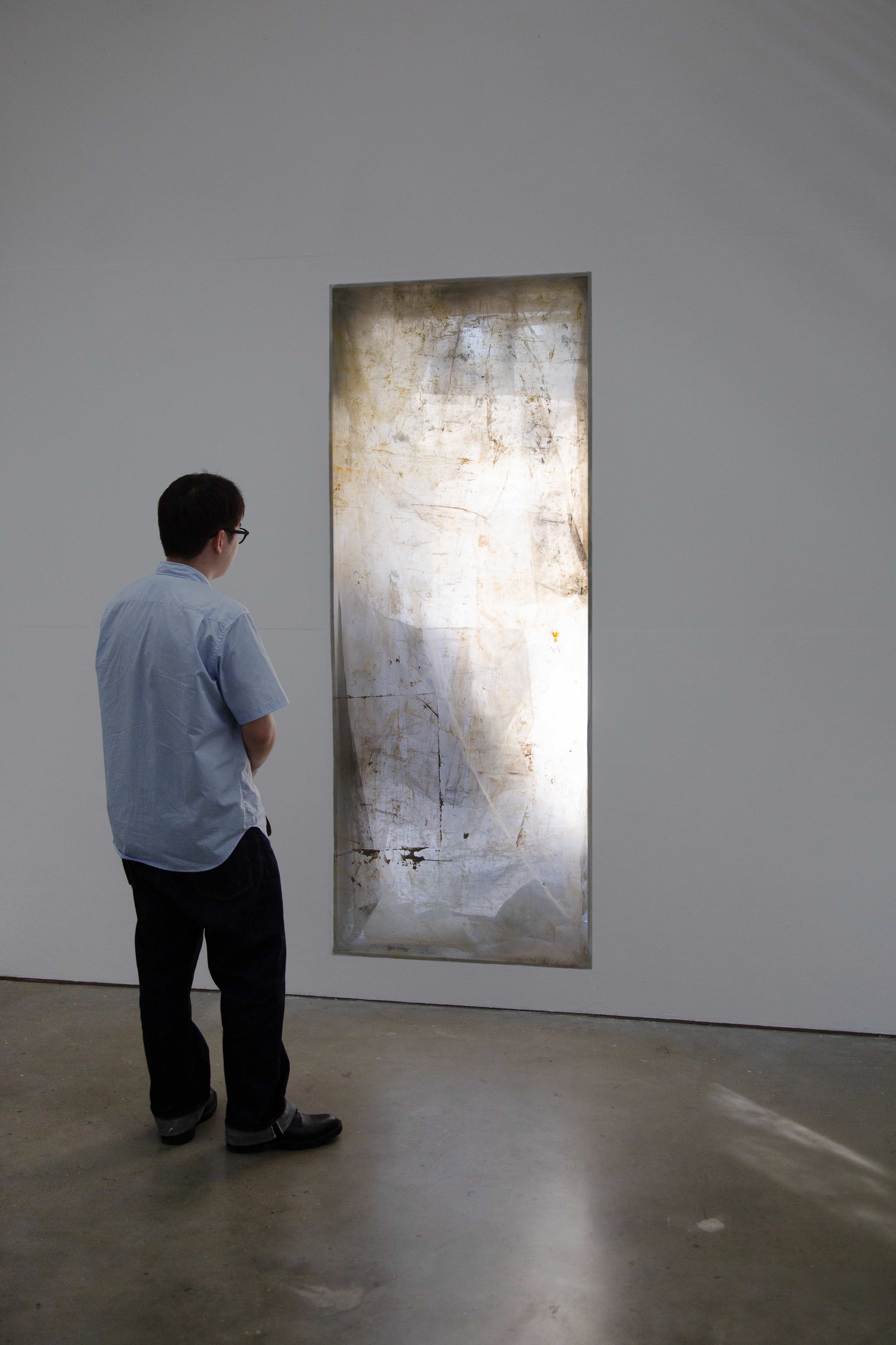 A long, vertical window covered in translucent layers of painted mesh screens, giving the appearance of a glowing impressionist painting.